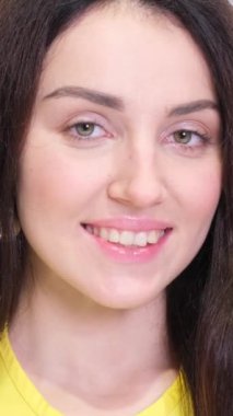 Stüdyoda beyaz bir arka planda güzel bir esmerin portresi, neşeyle gülüyor. Mutlu kız suratı, yakın plan. Dikey video