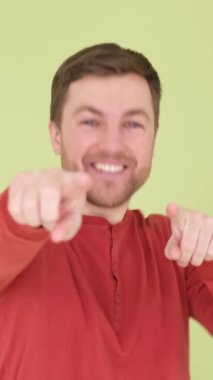 Yakışıklı bir adam kamerayı işaret eder, stüdyonun arka planında durur ve samimi bir şekilde gülümser. Bir adamın samimi, neşeli duyguları. Dikey video