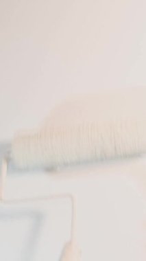 Dairede modern yenileme. Özel üniformalı bir adam dairesinin duvarlarını silindirle boyuyor. Duvarlar beyaz. Dikey video