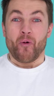 Mavi arka planda, stüdyoda kameraya bağıran mutlu bir adamın yakın çekimi. Neşeli ve duygusal. Dikey video