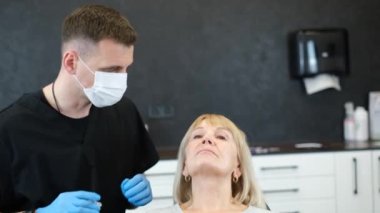 Bir kozmetolog yaşlı bir kadının gözlerinin etrafındaki deriye yaşlanmayı önleyici bir ilaç enjekte eder. Bir kozmetik uzmanı kozmetik kliniğinde iğne yapıyor, yakın plan. Dikey video