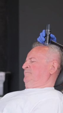Bir trikolog detaylı bir saç teşhisi koyar ve yaşlı bir adamı muayene eder. Saç tedavisi konsepti. Kellik ve saç kaybı. Dikey video