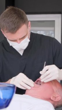Bir dişçi, dişçilik konsepti olan klinikte dişlerini muayene eden yaşlı bir adamla çalışır. Dikey video