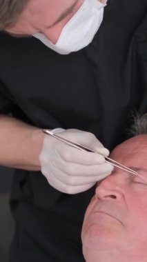 Cerrah, estetik ameliyattan önce yaşlı bir adamın yüzünü inceleyerek göz bölgesini değiştirir. Doktor estetik ameliyata hazırlanıyor. Dikey video