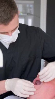Bir dişçi yaşlı bir adama modern diş implantları yerleştirir. Yaşlılıkta diş tedavisi. Sağlık hizmetleri. Dikey video