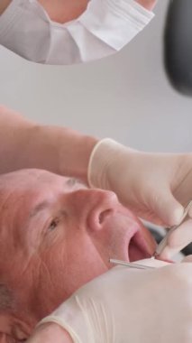 Üniformalı profesyonel bir diş cerrahı, modern aletlerle klinikteki yaşlı bir hastaya diş implantı takmak için ameliyat yapar. 4Dikey Video