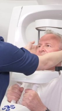 Doktor yaşlı bir insanın kafasının röntgenini çeker. Yüzünden estetik ameliyat hazırlığı. Dikey video
