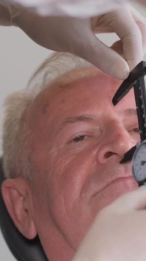 Doktor cerrahın portresi erkek yüzünde iz bırakıyor, yaşlı adam. Dikey video.