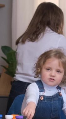 Anne mutfakta bulaşıkları yıkar ve kız masada oynar. Mutlu bir ailede uyum ve sevgi. Dikey video