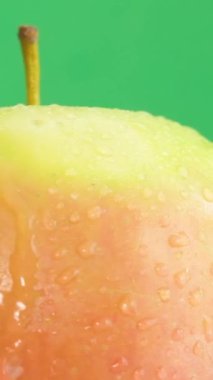 Üzerine su damlaları düşen taze bir elmanın güzel bir videosu. Yeşil arka planda dönen kırmızı ve sarı bir elma. Dikey video