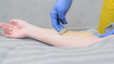 Ellerin deplasmanı. Güzellik uzmanının müşterinin eline epilasyon yaparken yakın plan fotoğrafı. Tüy dökümü için şeker ezmesi. Acısız bir epilasyon. Dikey video