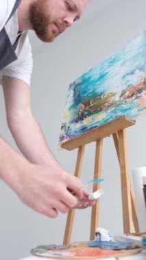 Profesyonel bir sanatçının beyaz bir tuvale fırça ve sehpa kullanarak resim yaptığı dikey bir video. Bir sanatçının bir resim yaratma süreci. Dikey video