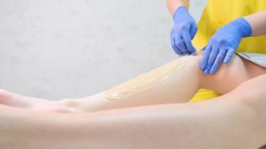 Bacak derisindeki kılları alma işlemi. Eldivenli bir güzellik uzmanı genç bir kadının bacaklarındaki kılları çıkarır. Dikey video