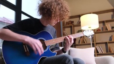Genç kıvırcık saçlı bir adam gitar çalmayı öğreniyor. Yetenekli bir gitarist sakin bir melodi çalar. Hobi olarak. Dikey video