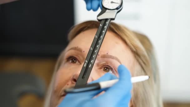 引退した女性を調べる プラスチック外科医の クローズアップ 彼はキャリパーを使います 古い年齢の顔の手術の概念 バーティカルビデオ — ストック動画