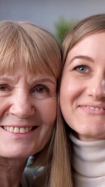 一个漂亮的金发姑娘和她妈妈的画像 他们看着相机笑着 快乐的家庭在家里休息 垂直录像 — 图库视频影像