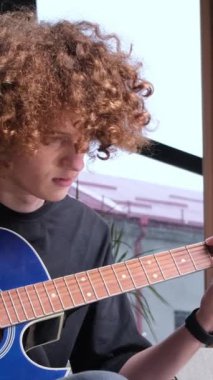 Amerikan görünümlü kıvırcık saçlı bir çocuk gitar çalmayı öğreniyor. Gitaristler yakın çekim yapar. Eğitim ve hobiler. Dikey video