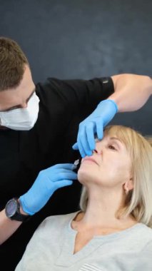 Yaşlı bir kadın için yüz gençleştirme prosedürü için Hyaluronic asit enjeksiyonları. Dikey video.