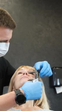 Bir doktor yaşlı bir kadını estetik ameliyata hazırlıyor. Estetik ameliyattan önce yüzünde delik var. Yüz estetiği konsepti. Dikey video