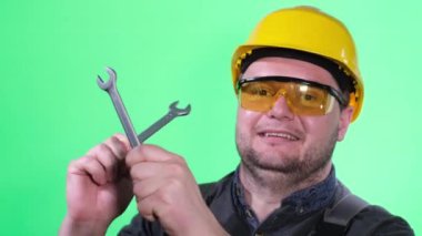 Kameraya gülümseyen bir oto tamircisinin portresi yeşil ekran arka planında bir ingiliz anahtarı tutuyor..