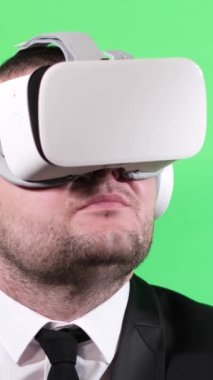 Stüdyoda yeşil arka planda sanal gerçeklik gözlüğü kullanan beyaz iş adamı. Dikey video