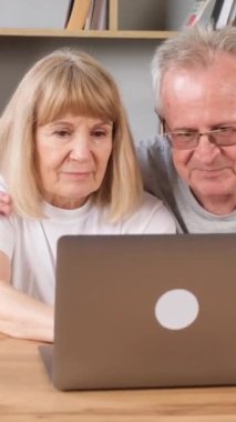 Oturma odasında dizüstü bilgisayarı olan mutlu yaşlı çift. Büyükbabam ve büyükannem birbirlerine aşıklar. Bilgisayarda bir şey arıyorlar. Dikey video