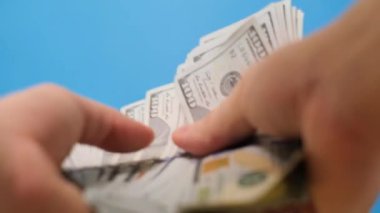 Avrupalı bir adamın mavi arka planda dolarla para sayarken yakın plan fotoğrafı. Aile bütçesi, nakit. Dikey video