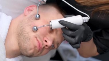 Dikey video kozmetik uzmanı iyontoforez prosedürü uyguluyor. Erkekler için yüz derisinin gençleşmesi. Modern kaplıca güzellik salonu. Dikey video