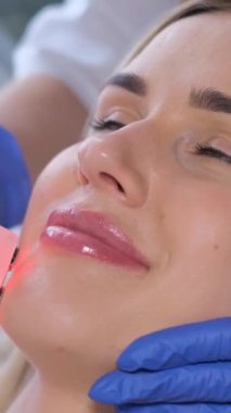 Güzel bir kadın kozmetik kliniğinde hiyalüronik asit jeli ile yüz fonofortesi ameliyatı geçiriyor. Güzellik endüstrisi konsepti. Dikey video
