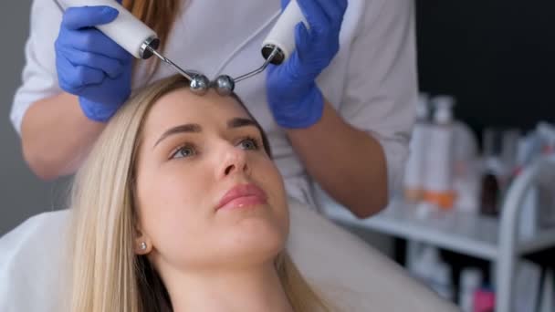美容師は顔の手順に電気パルスを使用しています 女性はマイクロカレント手順のフェイスリフトを取得します バーティカルビデオ — ストック動画