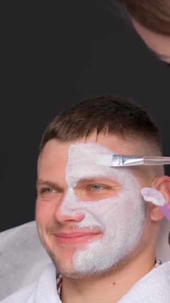 Młody Mężczyzna Spa Zabiegu Twarz Maska Gliniana Twarzy Kosmetolog Wykonuje — Wideo stockowe