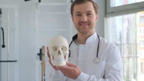 医者は人間の頭蓋骨を手に入れ カメラに微笑みかけている クリニックの神経科医の肖像画 バーティカルビデオ — ストック動画