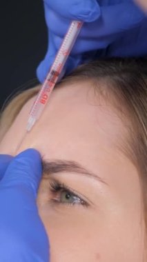 Kozmetik uzmanı bir kız güzellik salonunda güzel bir kızın dudaklarına ve yüzüne iğne yapar. Kozmetik kavramı. Dikey video