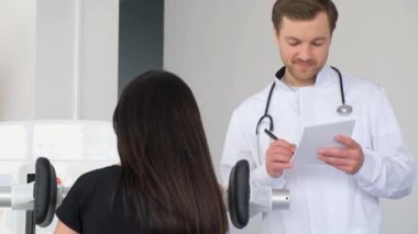 Genç bir kadın bir fizyoterapistle teşhis makinesinde omurilik muayenesi yapıyor. Osteokondroz, omurgalar arası bel fıtığı, omurgalar arası diskin çıkıntısı..