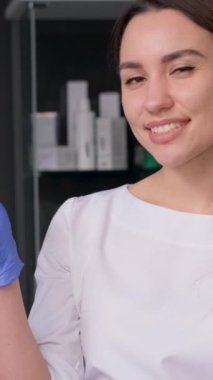 Ofisin ortasında duran ve kameraya gülümseyen güzel bir kadın güzellik uzmanı. Modern spa salonu. Dikey video