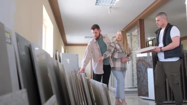 一对年轻夫妇正在和一个售货员谈论瓷砖商店的室内装饰 选择的概念 垂直录像 — 图库视频影像