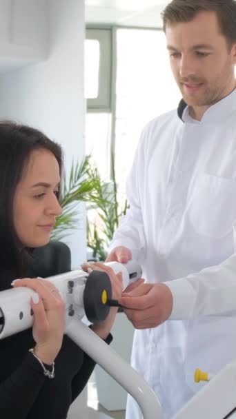 一位年轻妇女正在与理疗师一起在一台诊断机器上做脊柱检查 Vertebrology医院 垂直录像 — 图库视频影像