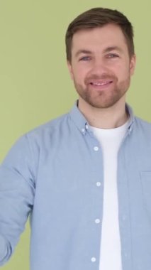 Çekici, neşeli, parlak yeşil arka planda izole edilmiş, tamam ilanı olan bir adam. Yaşam tarzı kavramları. Dikey video