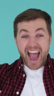 Mutlu kazanan adam, stüdyoda mavi arka planda zafer jesti göstererek seviniyor. Çocuk başarıyı ifade ediyor. Dikey video