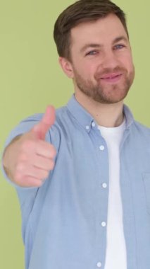 Neşeli, mutlu, gülümseyen genç adam yeşil arka planda parmağını kaldırmış kameraya bakıyor. İnsanların yaşam tarzı konsepti. Dikey video