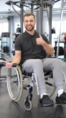 Rehabilitasyon sırasında spor salonunda çalışan tekerlekli sandalyedeki bir adamın dikey videosu. Özürlü insanlarda irade gücü. Dikey video