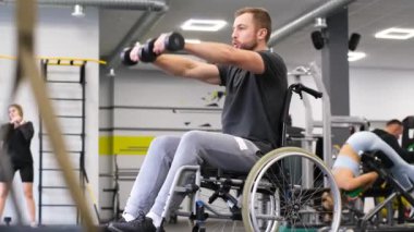 Tekerlekli sandalyedeki engelli bir adam spor salonunda dambılları kaldırıyor. Spor konsepti. Dikey video