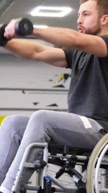 Tekerlekli sandalyedeki engelli bir adam spor salonunda dambılları kaldırıyor. Spor konsepti. Dikey video