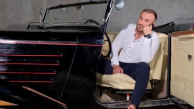 A young collector of retro cars is talking on a smartphone. Sale of retro cars.