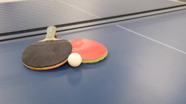 İki masa tenisi raketi mavi bir tenis masasında beyaz bir topu örtüyor. Masa tenisi. Çin halk sporları oyunu