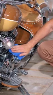 Motosikletin yanındaki garajda genç bir adam krom motoru parlayana kadar ovuyor. Güzel bir retro motosiklet. Dikey video