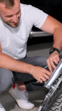 Sakallı bir adam yola çıkmadan önce motosikletinin frenlerini kontrol eder. Garajda bir motosikletin teşhisi. Hobi motorcusu. Dikey video