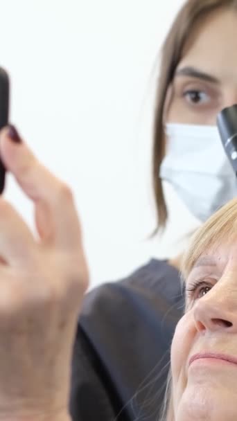 一位老年妇女的头皮由办公室里的一位三位一体的医生治疗 一位女性三叶草学家给病人剃头 并在手机上播放视频 垂直录像 — 图库视频影像