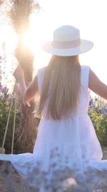 Çiçekler arasında güzel bir salıncakta sallanan bir kadının dikey videosu. Açık hava eğlencesi. Güzelliğin keyfi. Güzellik konsepti. Dikey video