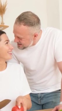  Genç bir kadın, kocası mutfakta ona sarılırken sağlıklı bir salata hazırlamak için sebze doğruyor. Dikey video